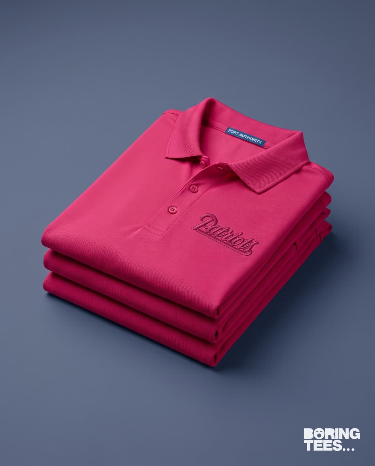 Folded stack of hot pink Port Authority polos with tonal Patriots script embroidery
