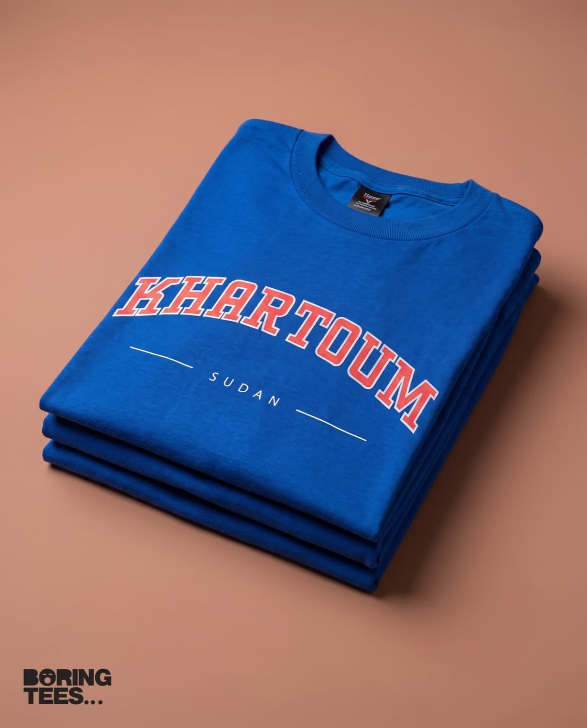 Folded stack of royal blue tees with KHARTOUM printed in red and white collegiate type
