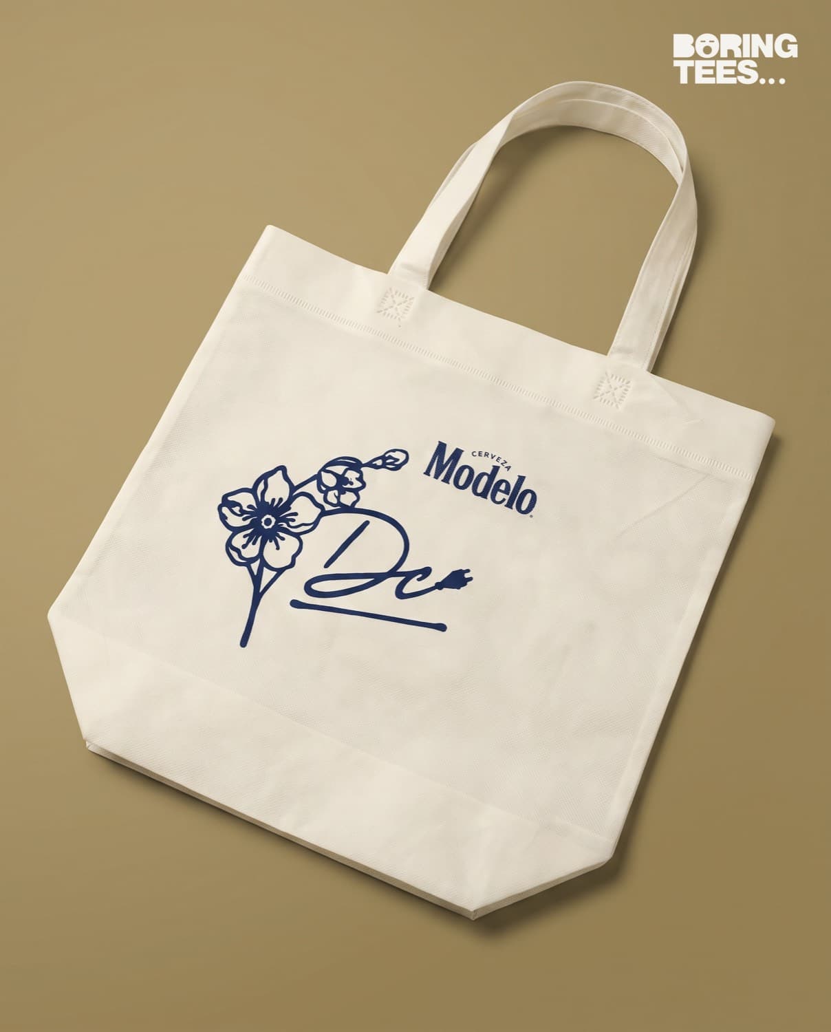 Natural canvas tote bag with a navy cherry blossom DC signature and the Cerveza Modelo logo
