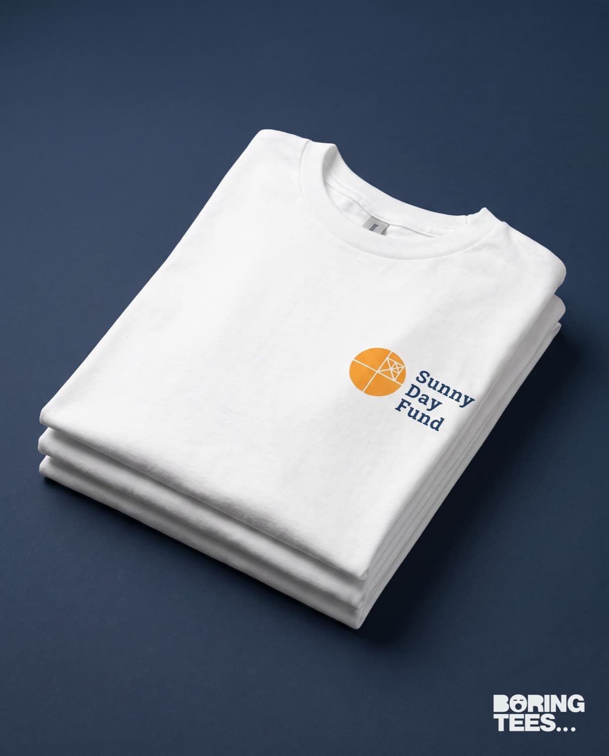 Folded stack of white tees with the navy and gold Sunny Day Fund logo on the left chest