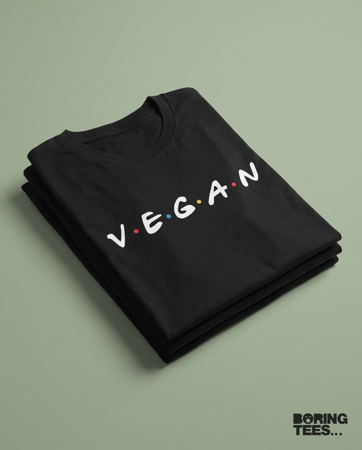 Folded black tees with V E G A N spelled out in white with coloured dots between the letters