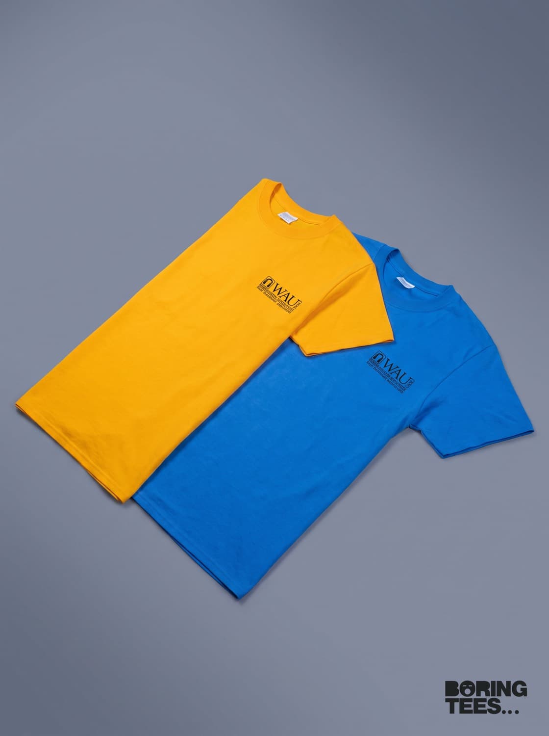 Gold and royal blue tees laid side by side, each with a small black Washington Adventist University lockup on the left chest
